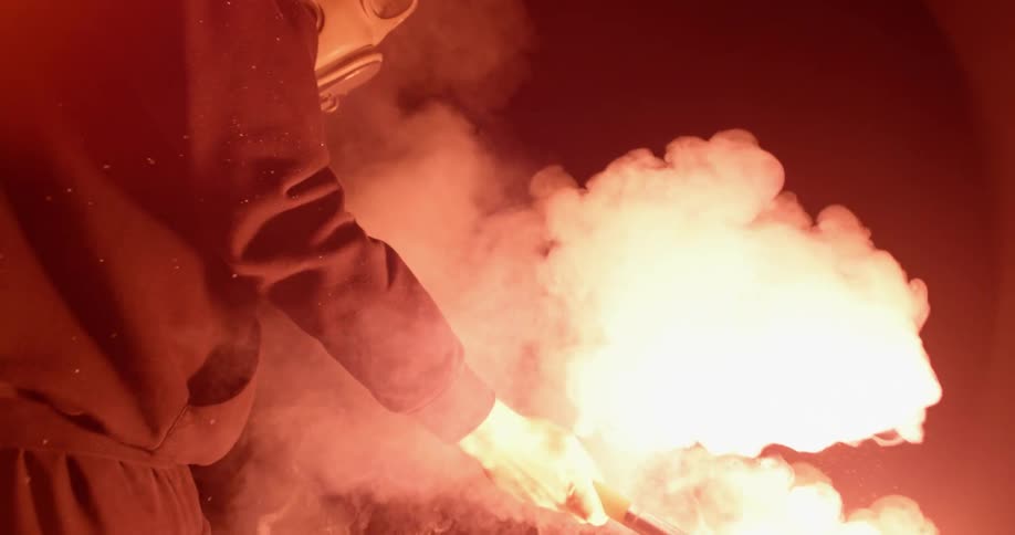 A man wearing a gas mask holds a lit flare