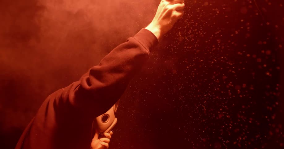 A man wearing a gas mask holds a lit flare