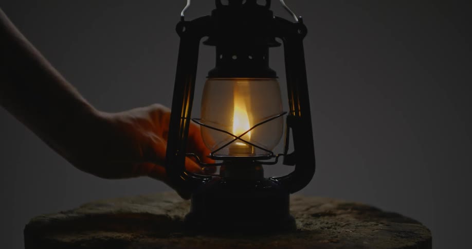 A hand adjusts the flame in an oil lamp