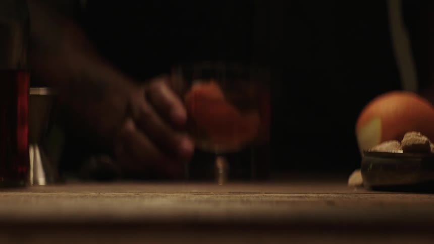 A man is rubbing the rim of a glass with an orange peel that has whiskey in it