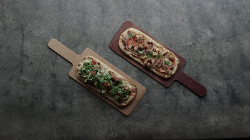 Two pizzas on wooden boards are put side by side for viewing