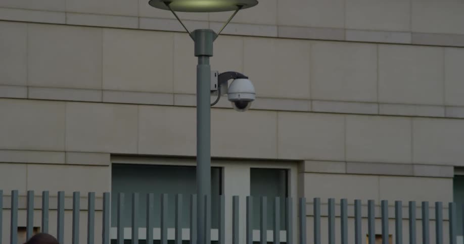 A security camera hangs on street light in front of city building