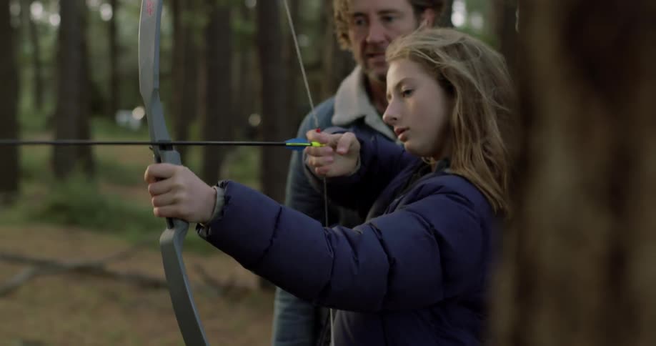 A man is teaching a girl how to draw a bow