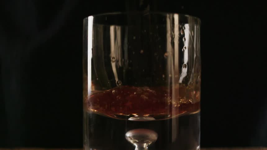 Liquor is poured into a glass and splashes up the sides