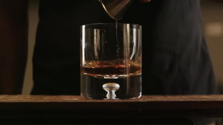 Person pours liquid from a shot glass into a bigger glass