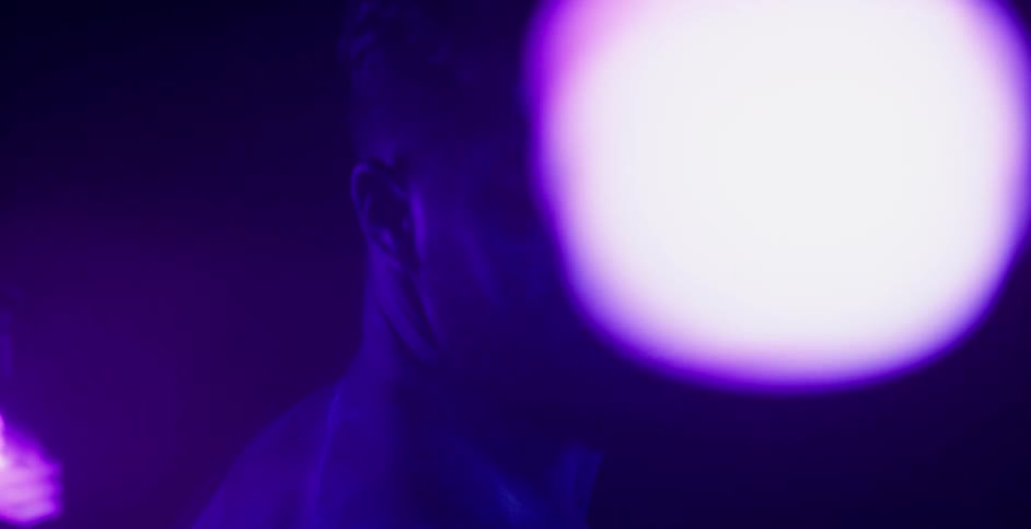 A light bulb dangles by a man covered in glowing body paint