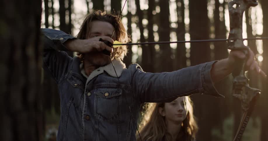 A man is teaching a young girl how to shoot a bow