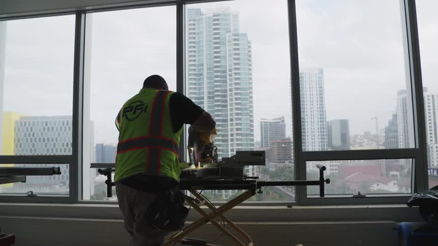 A man is cutting a piece of wood with a tall building in front of him