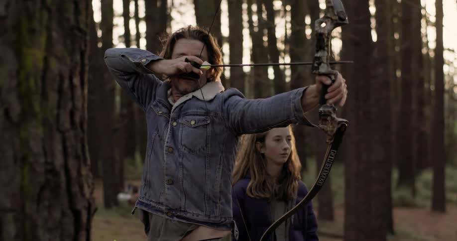 A man cocks a bow and fires into the woods