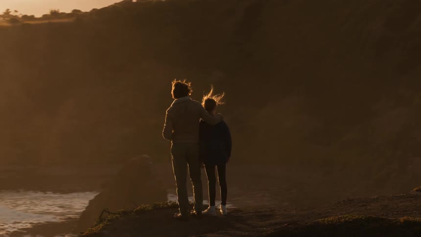 A man and girl overlook the ocean at sunset