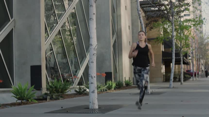 A female athlete is running down an urban sidewalk during the day