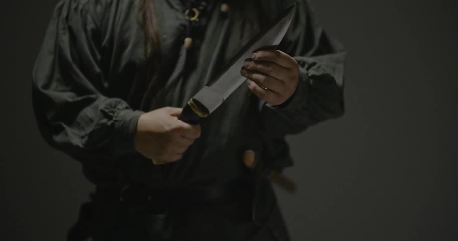 A man turns a knife over in his hands and then raises it