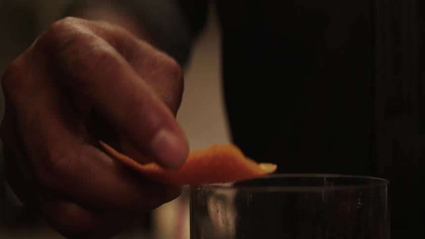 A bartender adds an orange peel to a drink