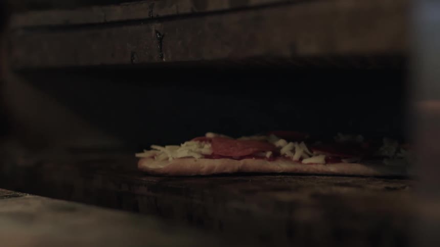 A pizza is slowly slit into a brick oven
