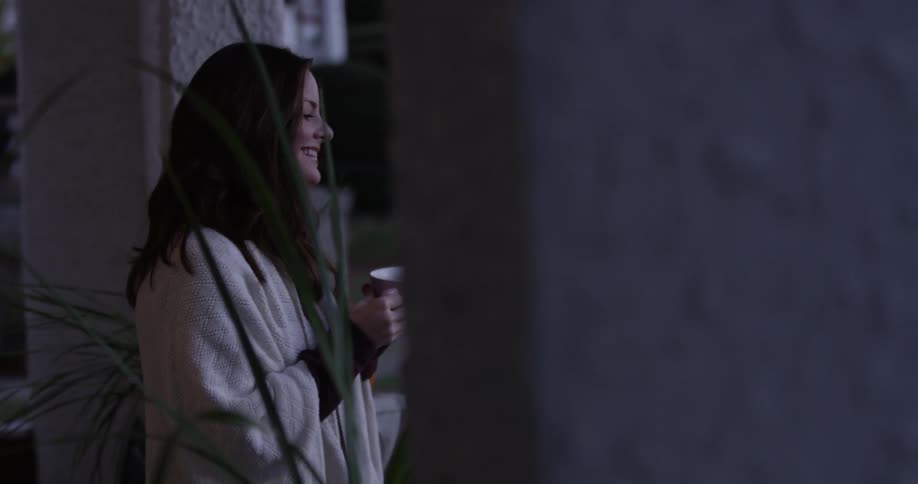 A woman is holding a cup of coffee on a porch