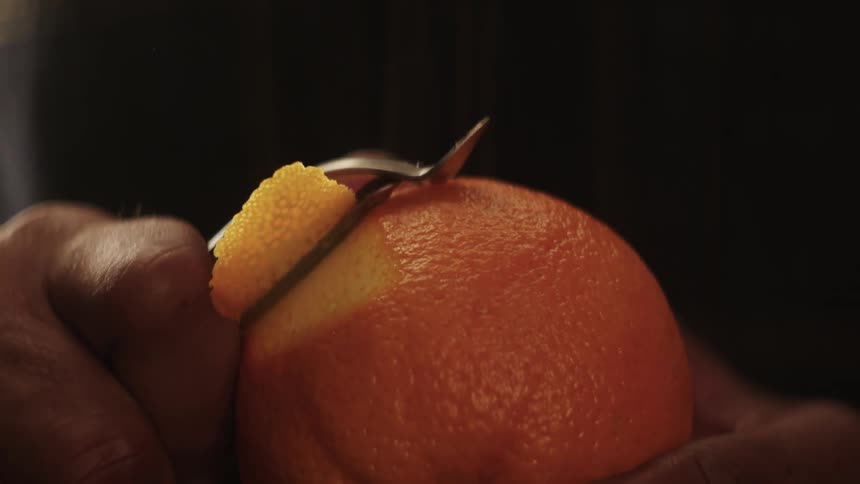 A man peels an orange with a vegetable peeler