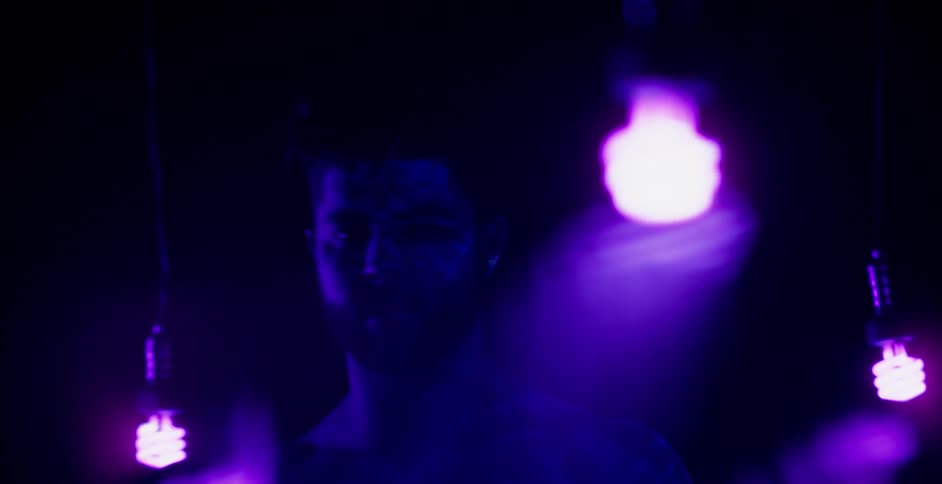 A man is covered in glowing body paint in a dimly lit room