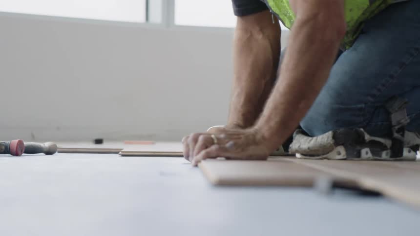 A construction worker applies adhesive to wood flooring