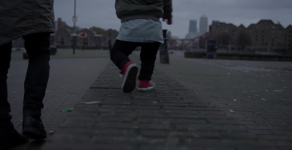 A toddler walks on a low brick wall while holding a man's hand