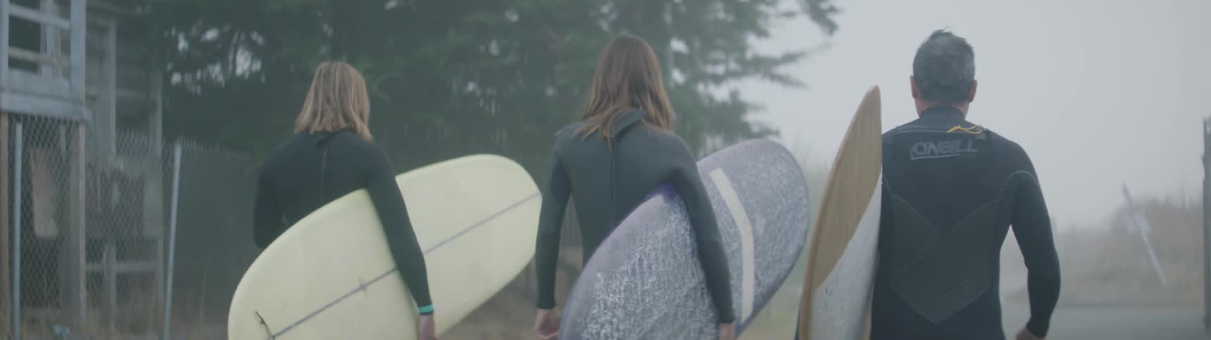 Three people walk towards the shore with surf boards