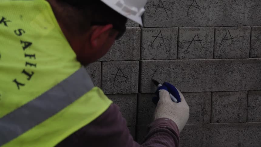 A worker writes on a stack of bricks using a sharpie