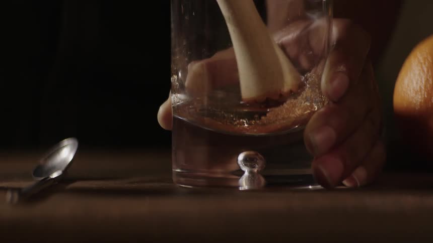 A bartender crushes up crystals in a liquor glass