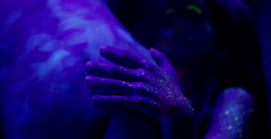 A man and woman embrace while covered in glowing body paint