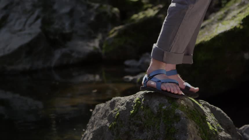 A person in sandals walks over large rocks