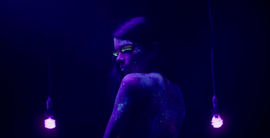 Lightbulbs dangle next to a topless woman covered in glowing body paint