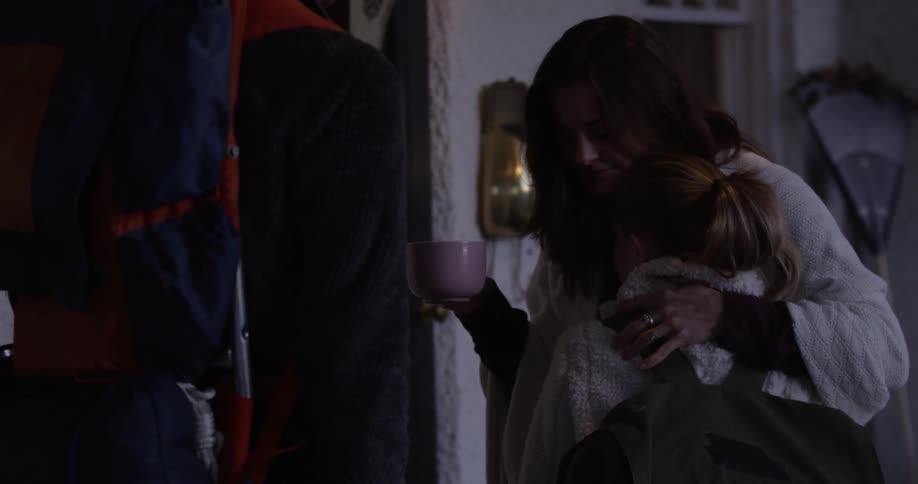Woman holding a mug hugs a young girl then kisses a man
