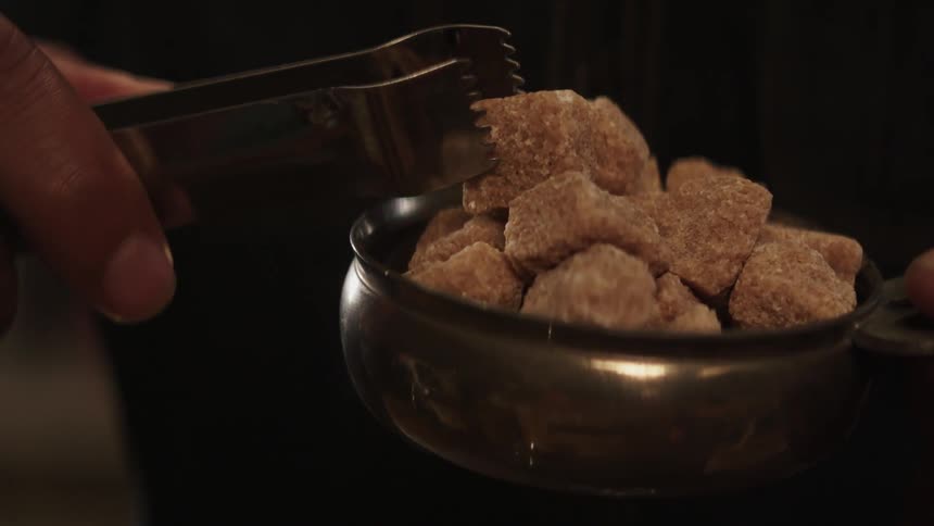 A bartender is getting a sugar cube with tongs
