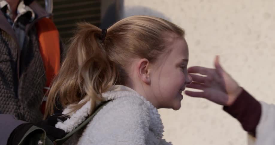 A little girl is putting on her backpack