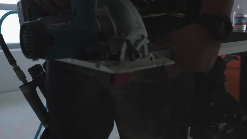 A man uses a saw to cut a piece of wood to length