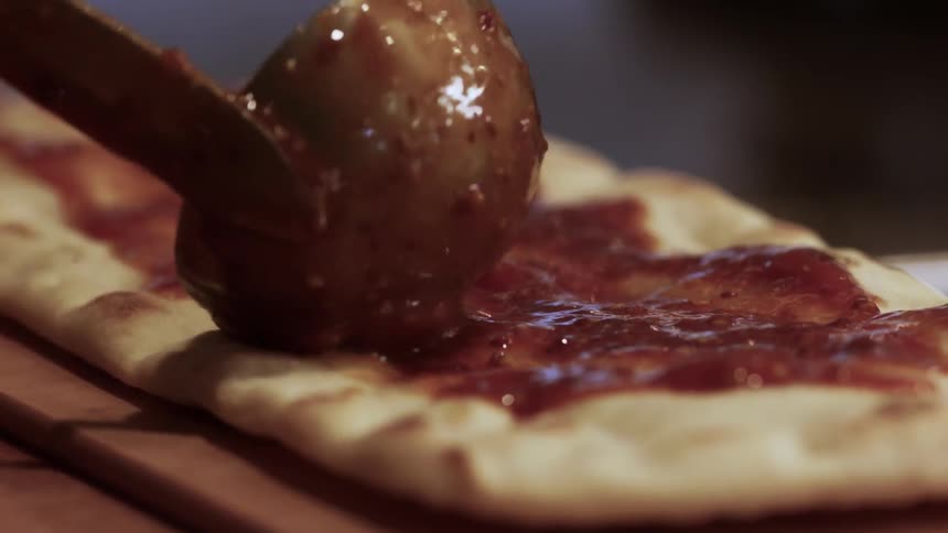 Someone is applying pizza sauce to a piece of flatbread
