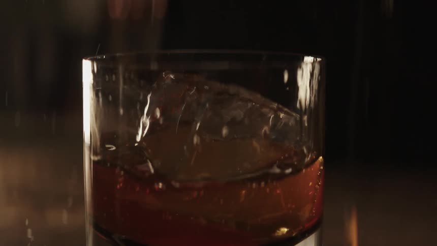 An ice cube is dropped into a glass of liquor