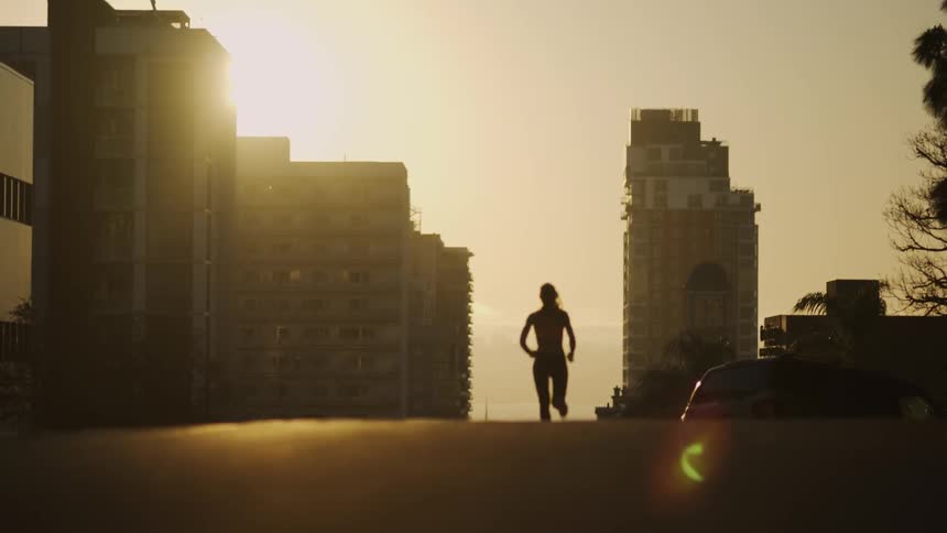 A woman is running up the street at sunset