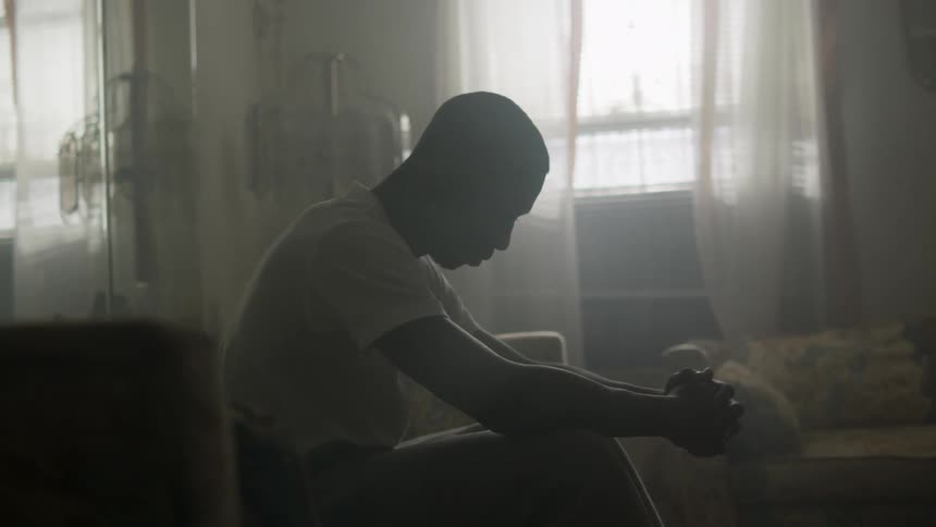A man sits in a living room holding his hands together
