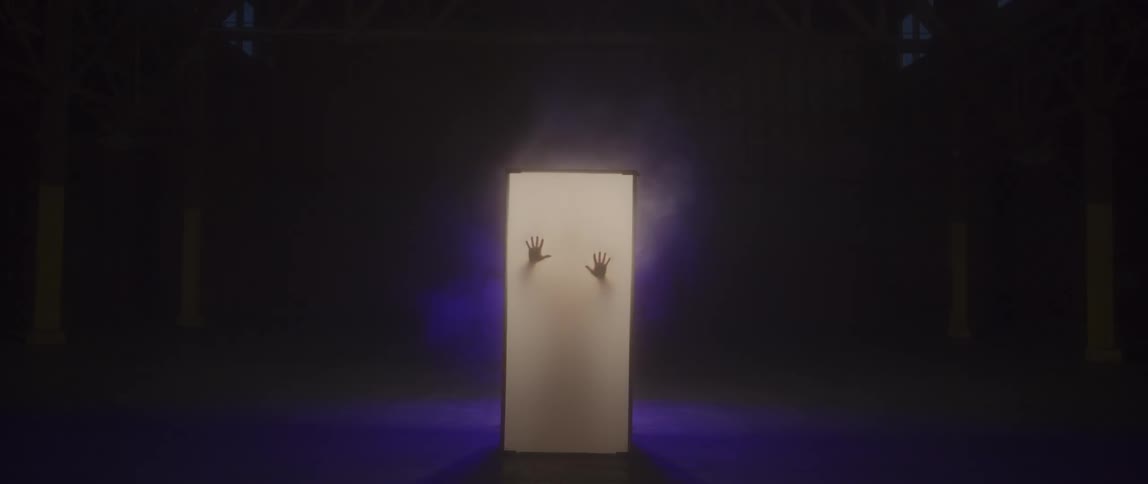 A silhouetted man stands in a glowing column and presses his hands against the wall