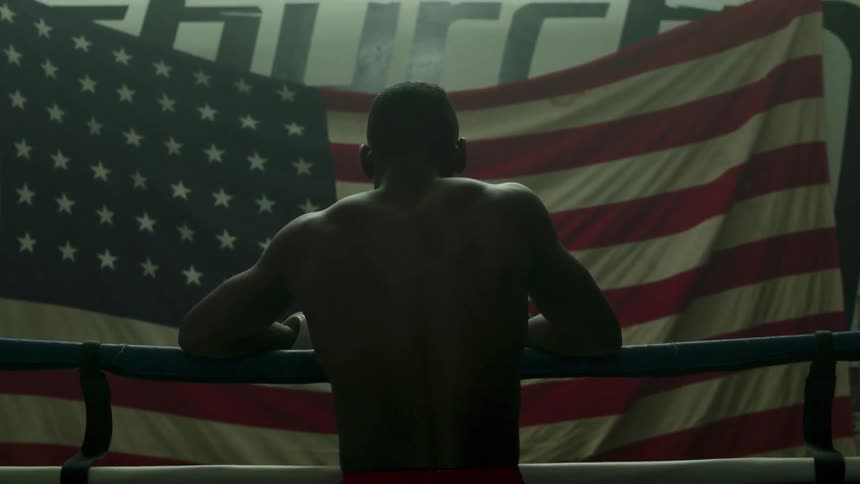 A man leans against the ropes in a gym