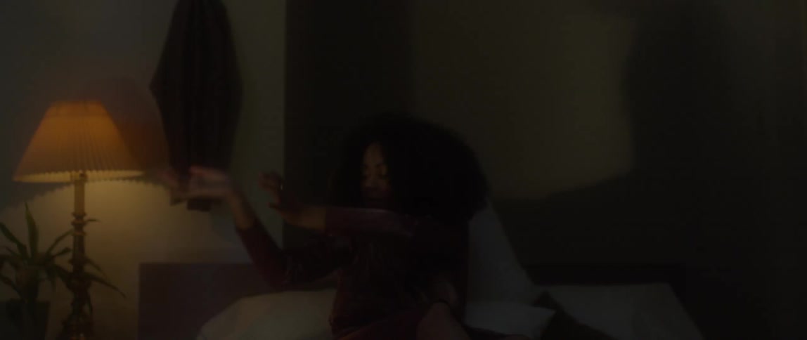 A woman gyrates abstractly while sitting on a bed