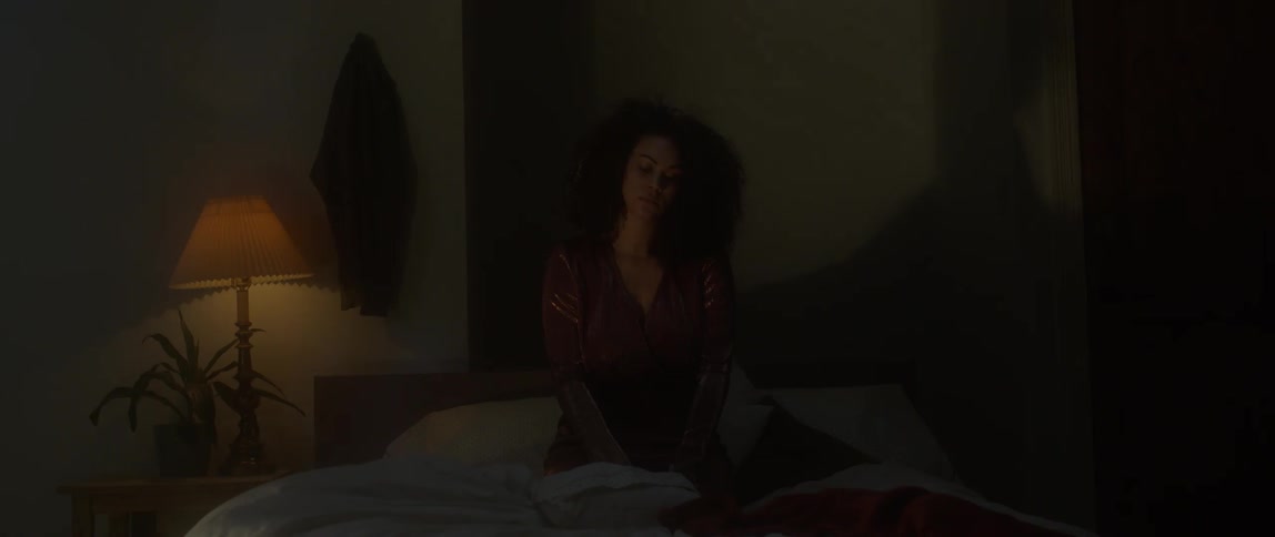 A woman sits on a bed in a dark bedroom