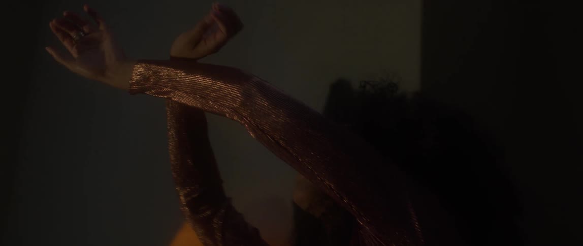 A woman swirls her hands as she sways in a dark room