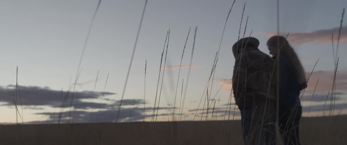 A man and woman stand together in a field