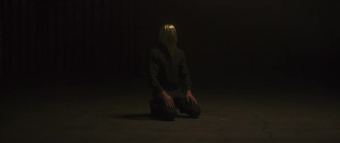 A person in a hood is kneeling in the dark