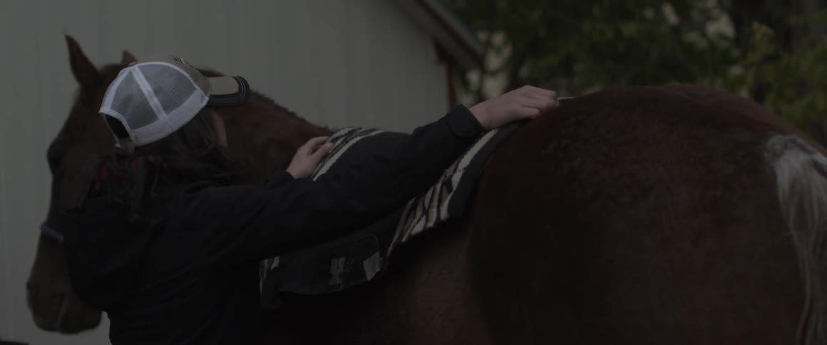 A woman puts a saddle on her horse