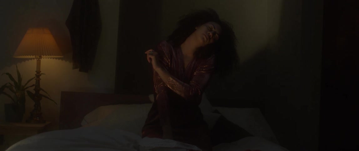 A woman kneeling on a bed rolls her head and stretches