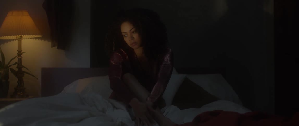 Light and shadow play on the face of a woman sitting on a bed in a dark room
