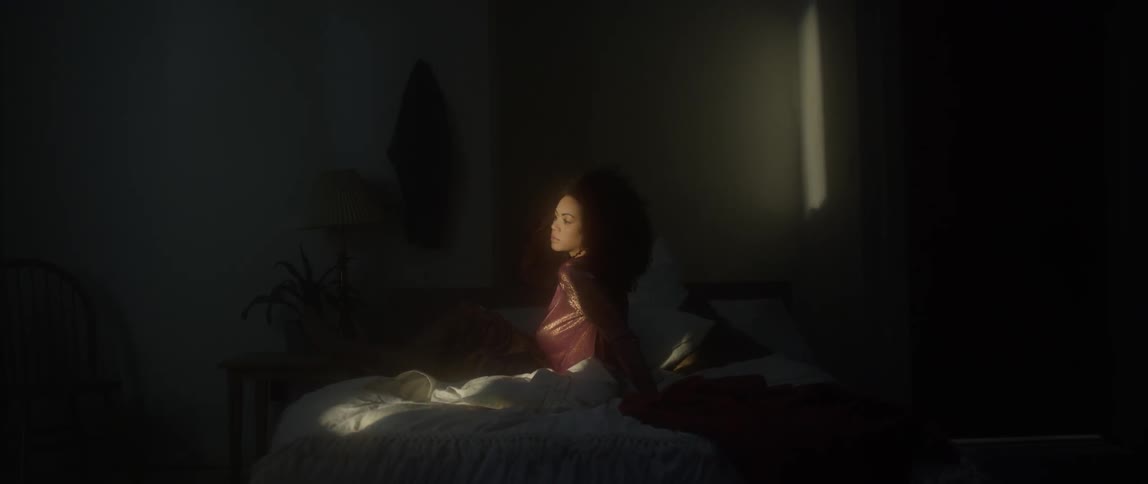 A woman sits on a bed in a dark room