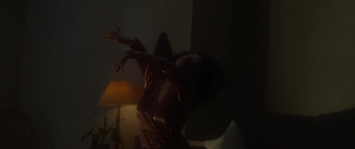 A woman dances and moves fluidly as she kneels on a bed
