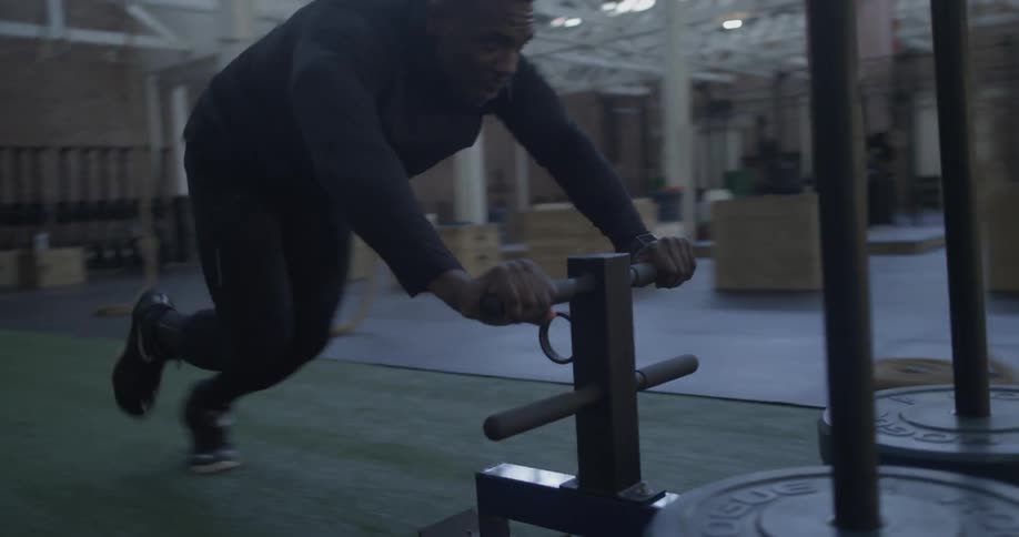 A man pushing weights on a cart across a gym floor